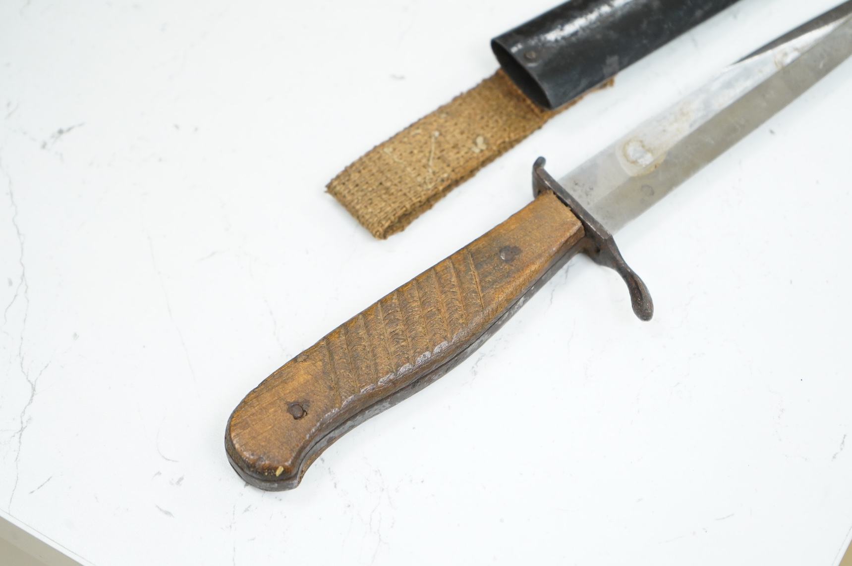 A First World War German Fighting Knife, with two piece wooden grip and steel cross guard, in original steel scabbard with canvas belt loop mount, single edged unmarked blade, blade 14cm, overall 25.5cm.